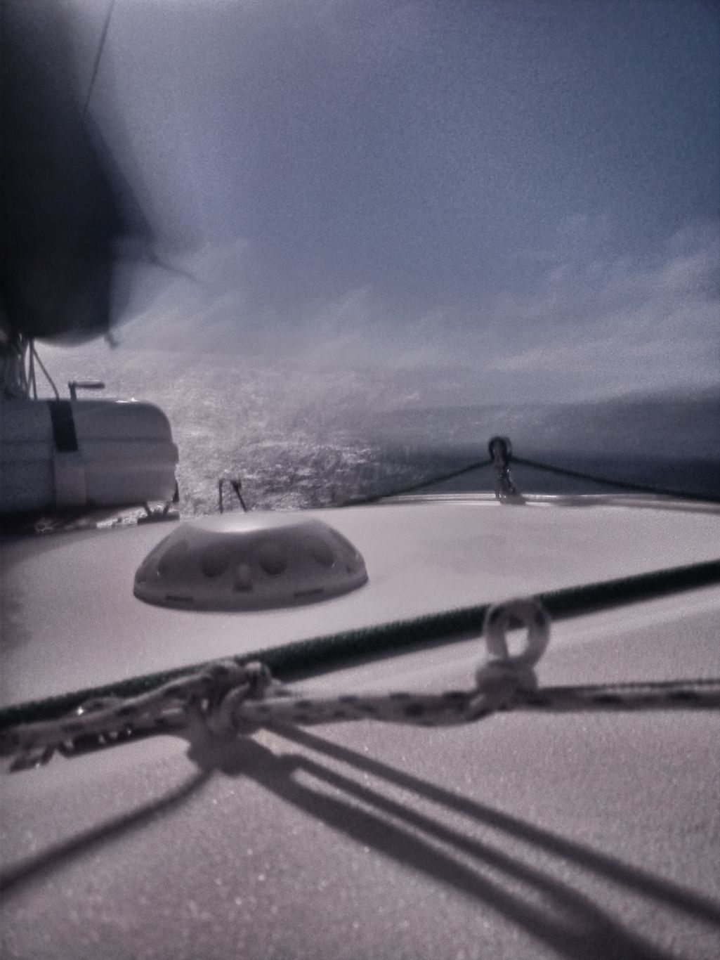 some knotted ropes across a deck with a vent and a boxed life raft, he background is haxy and indistinct as a result of a long exposure on a moving deck.